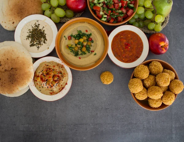 Authentic food of Middle East. Plate of hummus, falafels, pita bread, harissa sauce, tahini, fresh salad and fruits. Traditional meals of Israel top view photo. Colorful food picture.