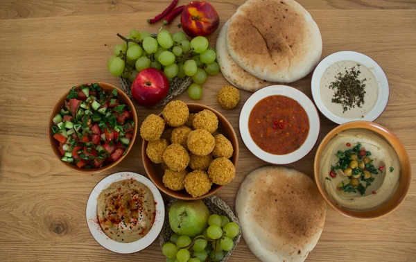 Authentic food of Middle East. Plate of hummus, falafels, pita bread, harissa sauce, tahini, fresh salad and fruits on wooden table. Traditional meals of Israel top view photo. Beautiful food picture with copy space.
