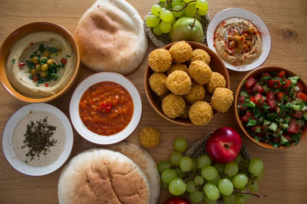 Authentic food of Middle East. Plate of hummus, falafels, pita bread, harissa sauce, tahini, fresh salad and fruits on wooden table. Traditional meals of Israel top view photo. Beautiful food picture with copy space.