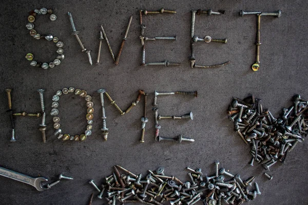 Home sweet home sign made of old bolts on dark grey textured background. Home renovation concept.