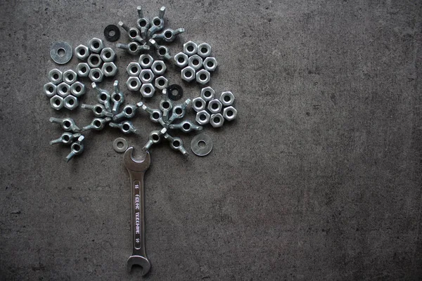 Bouquet made of old nuts and bolts. Old bolts and nuts on dark grey concrete background. Frame or border. Wrench tool, old nuts and bolts of different sizes top view photo. Grey textured concrete background with copy space.