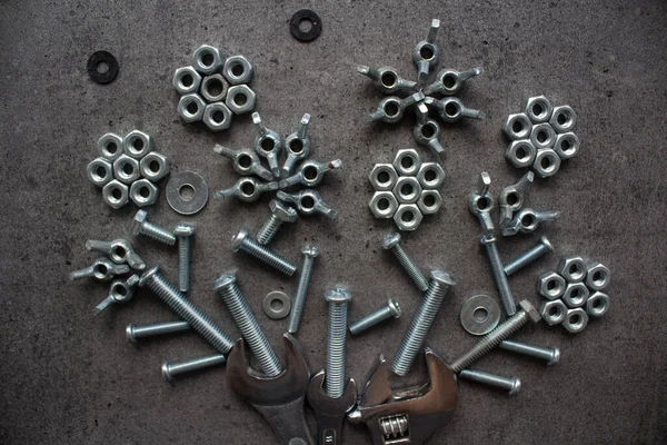 Bouquet made of old nuts and bolts. Old bolts and nuts on dark grey concrete background. Frame or border. Wrench tool, old nuts and bolts of different sizes top view photo. Grey textured concrete background with copy space.