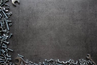 Eski civatalar ve fındıklar koyu gri beton arka planda. Çerçeve ya da sınır. Anahtar aleti, eski fındıklar ve civatalar farklı boyutlarda üst görüntü fotoğrafı. Fotokopi alanı olan gri desenli beton arka plan. Tamirci aletleri resmi kapatır. Ev yenileme konsepti.