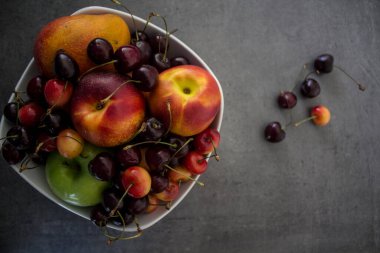 Kirazlı, şeftalili, elmalı ve mangolu beyaz vazo. Fotokopi alanı olan gri beton arka plan. Sulu yaz meyveleri ve meyveli üst manzara fotoğrafı. Sağlıklı yeme kavramı. 