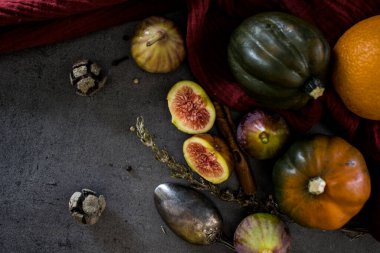 Koyu gri masada taze sonbahar sebzeleri ve meyveler. Mücevher kabağı, erik, sulu incir, biberiye ve gümüş kaşık fotoğrafı. Arka planda kırmızı desenli pamuk havlu. 