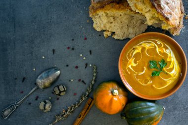 Gri masada taze ekmek ve gümüş kaşıkla balkabağı çorbası. Vejetaryen yemeğinin en iyi görüntüsü. Sağlıklı beslenme konsepti. Kopya alanı ile koyu desenli arkaplan. 