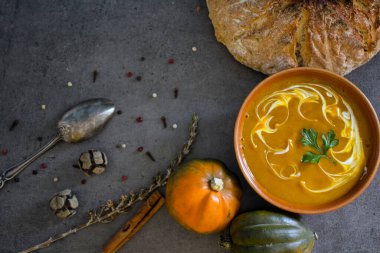 Gri masada taze ekmek ve gümüş kaşıkla balkabağı çorbası. Vejetaryen yemeğinin en iyi görüntüsü. Sağlıklı beslenme konsepti. Kopya alanı ile koyu desenli arkaplan. 