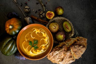 Gri masada taze ekmek ve gümüş kaşıkla balkabağı çorbası. Vejetaryen yemeğinin en iyi görüntüsü. Sağlıklı beslenme konsepti. Kopya alanı ile koyu desenli arkaplan. 