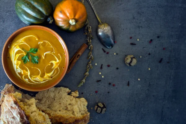 Pumpkin soup with fresh baked bread and silver spoon on gray table. Top view photo of vegan meal. Healthy eating concept. Dark textured background with copy space.
