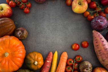 Kabakların, havuçların, elmaların, kiraz domateslerinin ve fotokopi alanı olan gri arkaplanda kırmızı soğanın en üst görüntüsü. Taze sonbahar sebzelerinden yapılmış renkli çerçeve veya sınır. 