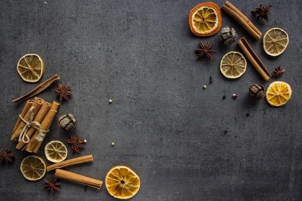 Border or frame made of dried lemons and oranges, cinnamon sticks, anise stars. Dark grey textured background with copy space. Autumn decoration.