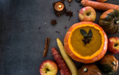 Kabak kabağında kabak çorbası. Arka planda gri dokuma ve fotokopi alanı. Anasonlu, biberiyeli, tarçınlı ve gümüş kaşıklı sonbahar yemeklerinin en iyi görüntüsü..