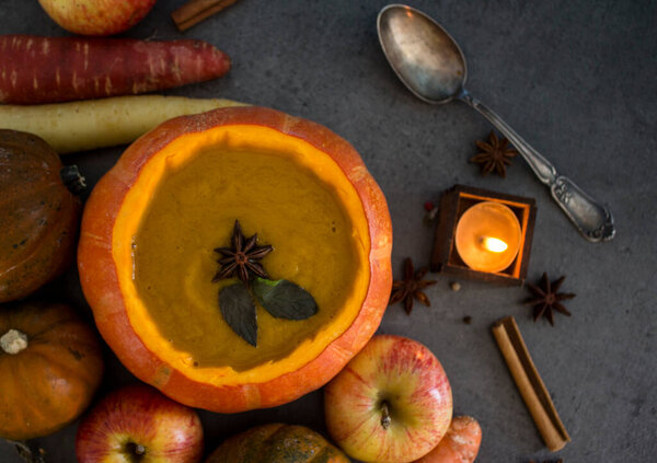 Squash soup in pumpkin bowl. Top view photo of pumpkin, apples, carrots anise stars and cinnamon sticks. Grey background.Autumn food close up photo. 