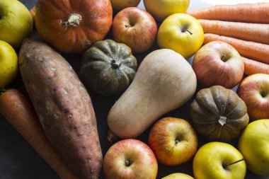 Sonbahar hasadı. Gri masada taze sebzeler. Tereyağı, ceviz kabağı, balkabağı, altın külçe, havuç, tatlı patates, elma. Sağlıklı yeme kavramı.