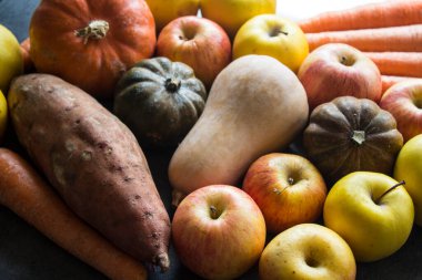 Sonbahar hasadı. Gri masada taze sebzeler. Tereyağı, ceviz kabağı, balkabağı, altın külçe, havuç, tatlı patates, elma. Sağlıklı yeme kavramı.