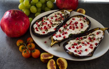 Beyaz tabakta kavrulmuş patlıcan, masada nar ve üzüm. Akdeniz tarzı yiyecekler. 