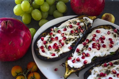 Beyaz tabakta kavrulmuş patlıcan, masada nar ve üzüm. Akdeniz tarzı yiyecekler. 