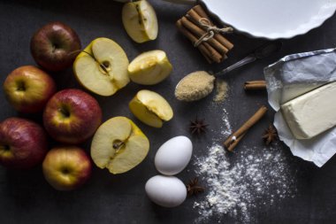 Elmalı turta malzemesi, en iyi görüntü fotoğrafı. Kırmızı elmalar, yumurtalar, tarçın çubuklar, tereyağı ve kahverengi şeker bir masada.