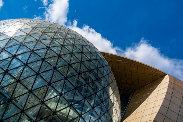Modern stylish office building. Rounded geometrical shapes with golden checkered pattern. Glass dome with triangular glazing and black metal frames. Unique design elements. 