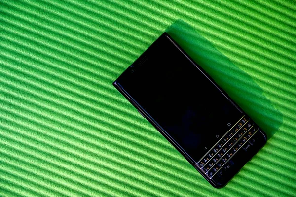 Modern işletme akıllı telefonu yeşil çapraz çizgili bir yüzeyde duruyor. Uluslararası qwerty klavye ile acımasız siyah cihaz, katı, hatta sert tasarım.