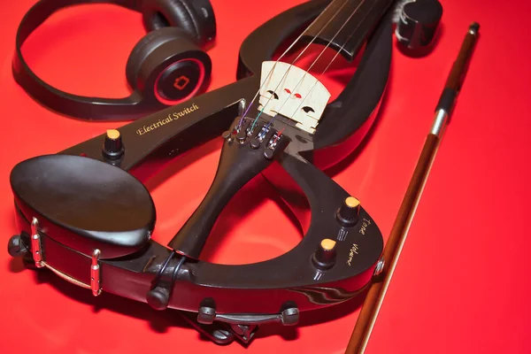 Detail electric violin with bow and headphones on a red background and in horizontal position.