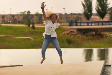 Beyaz gömlek ve kot pantolonla sevinçten havalara uçan genç sarışın kadın..