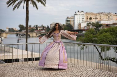 Genç bir kadın, İspanyol, güzel, esmer, zarif bir menekşe elbisesi olan, elbisesini uçurmak için komik kıvrımlar yapan. Güzellik kavramı, moda, trend, zarafet, antika.