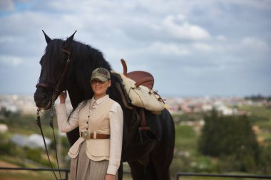Genç bayan binici, siyah İspanyol safkan atının yanında poz veriyor, dizginleri elinde tutuyor. Konsept at biniciliği, at biniciliği, binicilik, binicilik.