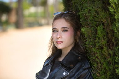 Genç bir kadının portresi, güzel, sarışın, yeşil gözlü, deri ceketli ve güneş gözlüklü, kameraya tatlı ve hassas bakıyor. İsyankar, boyun eğmez, isyancı konsept.