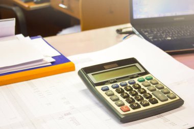 Hesap makinesindeki odak noktasını, iş konsepti görüntüsünü seçin. Bilgisayarlı ve hesap makineli ofis iş yerinin görünümünü kağıt kağıtlı ve rakamlı tabloda seçin.