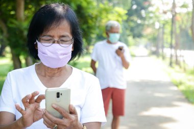 Yaşlı çiftler, virüsün yayılmasını önlemek için telefonda bez maskeler takıyorlar. Coronavirus Önleme Konsepti, Sosyal Mesafe. Boşluğu kopyala
