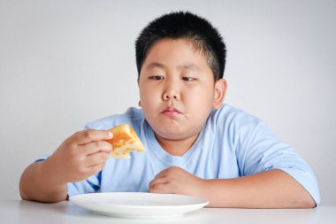 Şişko çocuk çok kilo almış, pizza yiyor.