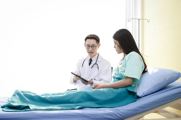 Asian male doctors use a stethoscope to check the heart rhythm of a female patient lying in a hospital bed. Concepts of health examination and medical services