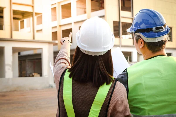 Systems architects and engineers stood looking at the blueprints at the building construction site to check for accuracy. Urban development technology concepts