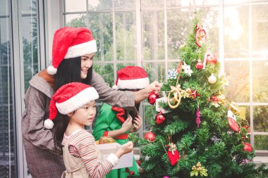 Kırmızı Noel Baba şapkası takan güzel bir kadın ve küçük bir kız Noel ağacını süslüyorlar. Mutlu Noeller ve mutlu tatiller