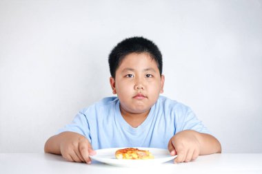 Şişko çocuk beyaz bir masada dinlenen bir pizza tabağı tuttu..