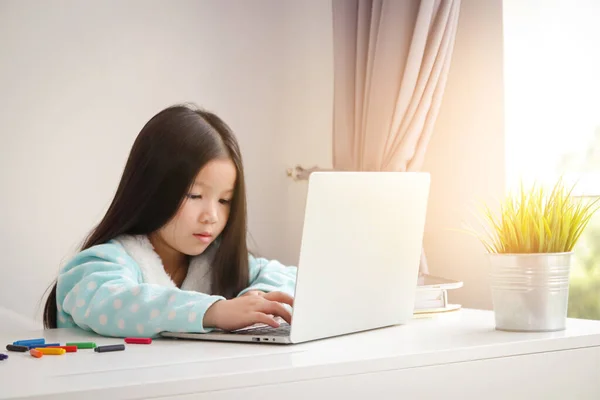 一个留着长发的小女孩 在家里的白桌子上 用笔记本电脑观看在线媒体 互联网 — 图库照片