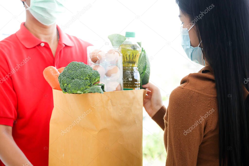 Delivery staff wearing red shirts. Give the bag of fresh food to the girl in front of her house. Online shopping concept during covid19, prevention of virus infection, social distance