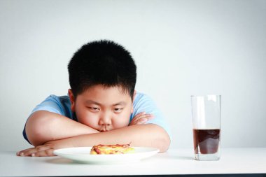 Şişko Asyalı çocuk pizzaya yemek için büyük bir arzuyla baktı. Çocuk sağlığı kavramı