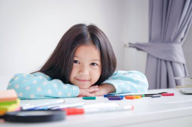Uzun saçlı şirin Asyalı çocuklar, resim çizmeyi ve resim yapmayı seviyor. Beyaz masasında mutlu bir gülümseme