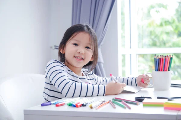 这个亚洲小女孩在客厅的白桌子上画画 她从小就喜欢学习和练习艺术 — 图库照片