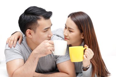 Sevgililer yatağa uzanıp bir fincan kahve içerler. Yatak odasında mutlu mesut konuşurlar. Beyaz arka plan. Yeni evli çift kavramı.