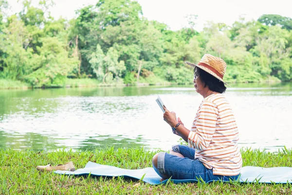 一位老妇人在一个有一个大池塘的公园里看书 退休后 她过着幸福而简朴的生活 高级社区概念 — 图库照片