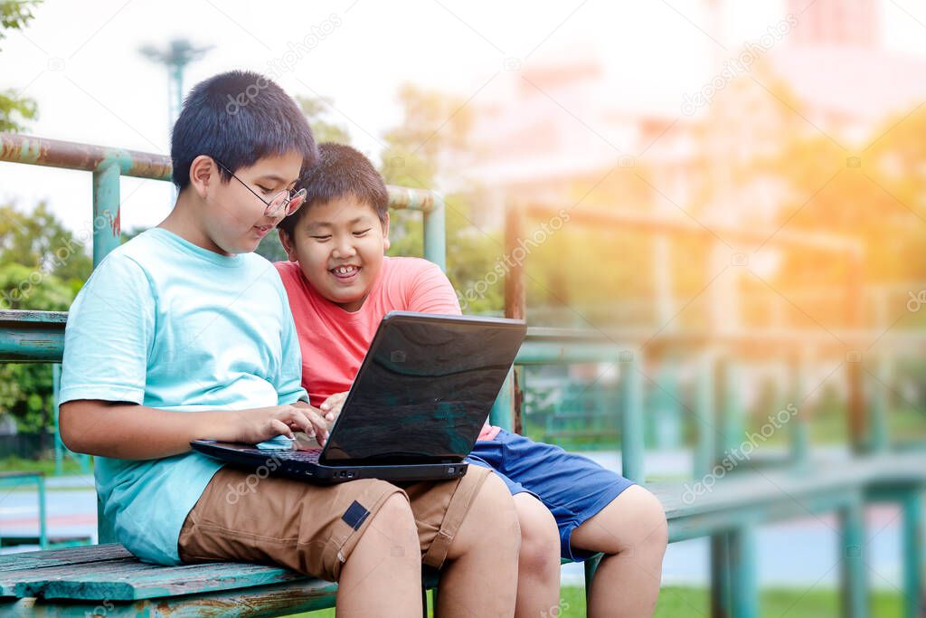 Two boys are watching the computer at the playground, both smiling and laughing.