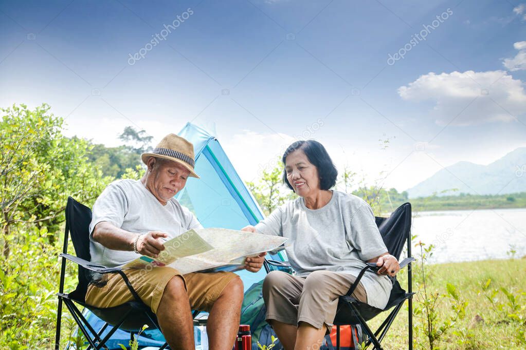 Happy asian senior couple Camping at the waterfront, sitting on a chair, view tourist map, with copy space.