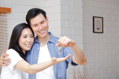 Asyalı çiftler yeni bir evde birbirlerine sarılıyorlar. Erkekler ev anahtarlarını kadınlara veriyorlar. Mutlu bir aile kurma kavramı. Boşluğu kopyala