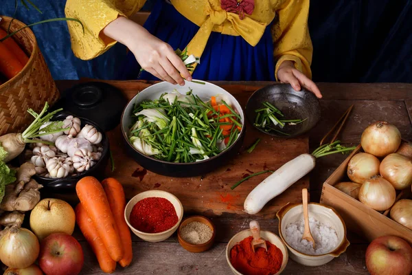 Asian women wearing hanbok, a Korean national costume, cook traditional kimchi, fermented cooking. Scented Including carrot, white cabbage, onion, cayenne pepper, garlic, salt, radish, apples — Stock Image Asian Women Wearing Hanbok Korean National Costume Cook Traditional Kimchi Stock Image