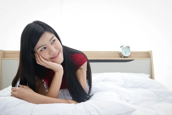 A beautiful Asian woman lounging in bed in the bedroom and smiling, happy holidays. Copy space