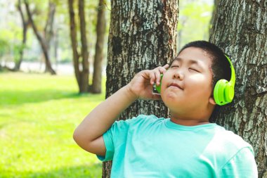 Yeşil kulaklık takan çocuklar ağaca yaslanmış, gözleri kapalı, mutlu