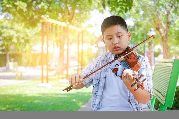 小学的亚洲男孩在公园里拉小提琴 — 图库照片